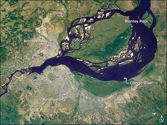 This astronaut image shows two capital cities (brownish-gray areas) on opposite banks of the Congo River. The smaller city on the north side of the river is Brazzaville, while the larger, Kinshasa, is on the south side. The cities lie at the downstream end of an almost circular widening in the river known as Stanley Pool. The international boundary follows the south shore of the pool (roughly 30 km in diameter). The Republic of the Congo, originally a French colony, is sometimes called Congo-Brazzaville - as opposed to the Democratic Republic of the Congo (known from 1971 to 1999 as Zaire) which is often called Congo-Kinshasa, originally a Belgian colony. Brazzavilles population is less than a tenth of Kinshasas. There is no bridge between the cities so that water craft of many kinds ply between them. It is not uncommon to see dugout canoes being paddled between the cities. Photo courtesy of NASA.